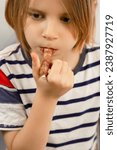 Small photo of Tasty intermission: A long-haired 10-year-old takes a break, savoring a sausage snack