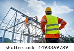 Small photo of Engineer technician watching team of workers on high steel platform,Engineer technician Looking Up and Analyzing an Unfinished Construction Project.