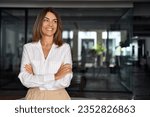 Beautiful hispanic senior business woman with crossed arms smiling, looking aside. European Latin confident mature good looking middle age leader female businesswoman on office background, copy space.