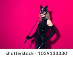 Beautiful dominant blonde vamp mistress girl with fashion makeup in glamour latex dress, collar, corset and bdsm black leather fetish cat mask posing on hot pink backgroung
