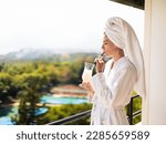 Small photo of Young millennial woman in white bathrobe spa girl on a balcony drinking a non alcoholic milk lactose free Pina colada cocktail vacation mood during summer. Travel relax time