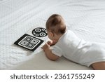 Small photo of A baby looks at a black and white contrast educational book. Intellectual development of newborns. Developing cards for children.