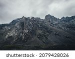 Small photo of Dark atmospheric landscape with rocky mountain wall under gray cloudy sky. Rocky pinnacle in lead gray cloudy sky. Dark mountain peak in overcast weather. Gloomy minimalist scenery with high mountains
