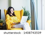 Young Indian woman using her laptop at home while sitting on a yellow armchair