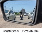 Small photo of The reflection of a motorcycle in the left side mirror of a car traveling in traffic and preparing to overtake between two cars in a narrow side distance at speed. Provoking a traffic incident.