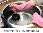 Small photo of woman's hands with a plunger unclogging the kitchen drain because it is clogged with leftover food. need plumber