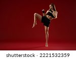 Female trainer showing kick exercise for self defence by legs on red background. Front view of attractive woman training in black sport bandages in studio. Concept of box.