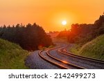 The setting sun against the background of the international railway line passing through the forest. Sunset lighting. Winding road. Railway infrastructure.