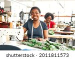 Small photo of Two black African Zimbabwean ladies working in a textile factory on the sewing line using sewing machines, measuring tapes and scissors to stitch lining in African styled patterned fabric garment