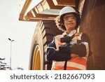Small photo of A young African woman mine worker is standing in front of a large haul dump truck wearing her personal protective wear