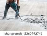 Worker at construction site demolishing concrete with electric jack hammer.