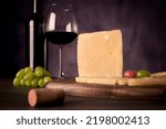 Small photo of A piece of Manchego Cheese from Spain with some green and red grapes and a glass and bottle of Spanish red wine at the background in a dark food photography style