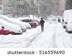 Snowstorm and snow-covered street and cars with a lonely pedestrian