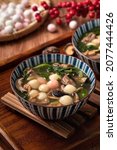 Small photo of Close up of red and white tangyuan (tang yuan, glutinous rice dumpling balls) with savory soup in a bowl on wooden table background for Winter solstice festival food.