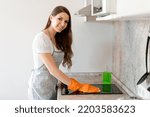 Young caucasian woman wiping an electric stove with a textile wipe while working in a modern kitchen at home. Cleaning service concept. Housework. Cleaning lady at work