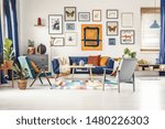 Small photo of Simple posters gallery hanging on the wall in bright living room interior with blue sofa, two armchairs, fresh plants and wooden coffee table standing on colorful carpet