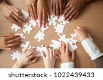 Hands of diverse people assembling jigsaw puzzle, african and caucasian team put pieces together searching for right match, help support in teamwork to find common solution concept, top close up view
