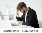 Depressed unsuccessful businessman feels terrible headache, distraught stressed entrepreneur regrets of business mistake shocked by bankruptcy desperate after failure sitting at work desk with laptop