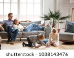 Children sister and brother playing drawing together on floor while young parents relaxing at home on sofa, little boy girl having fun, friendship between siblings, family leisure time in living room