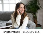 Smiling millennial woman talking on the phone at home, happy young girl holds cellphone making answering call, attractive teenager having pleasant conversation chatting by mobile with friend