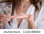 Small photo of Woman holding pill and glass of water in hands taking emergency medicine, supplements or antibiotic antidepressant painkiller medication to relieve pain, meds side effects concept, close up view