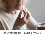 Mature senior middle aged woman holding pill and glass of water taking painkiller to relieve pain, medicine supplements vitamins, antibiotic medication, meds for old person concept, close up view