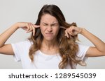 Stubborn annoyed woman sticking plug fingers in ears not listening to loud noise sound isolated on white blank studio background, young angry teen refuse hear avoid stress feel ear pain ache concept