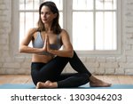 Young attractive woman practicing yoga, doing Half lord of the fishes exercise, Ardha Matsyendrasana pose with namaste , working out, wearing sportswear, pants and top, indoor full length, yoga studio