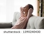 Side close up view serene young woman holds hands behind head closed eyes feels placidity, tranquil girl having day nap leaning on comfortable sofa in living room, refreshment and daydreaming concept