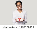 Smiling african American millennial woman in glasses isolated on grey studio background hold wrapped birthday present, happy biracial girl give gift box with red bow greeting with special occasion