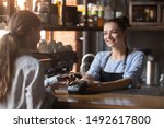 Female customer holding phone near nfc terminal make contactless mobile payment with smiling waitress barista saleswoman on coffeeshop counter, woman client pay in cafe with cellphone via pos machine