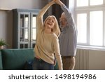 Overjoyed mature grey-haired Caucasian husband and wife have fun enjoy time together at home, happy elderly couple spouses dancing in living room, senior man lead sway smiling middle-aged woman