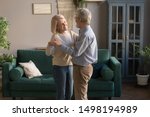 Small photo of Happy mature loving couple dancing in living room relaxing at home on weekend together, smiling grey-haired elderly husband and wife spend time waltz hugging embracing, spouses enjoy romantic date