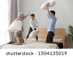 Happy multi 3 three generations men family old grandfather, adult son and little grandson having fun pillow fight on bed, young father with grandpa child boy laugh feel joy play funny game in bedroom