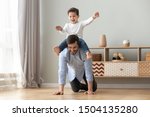 Happy funny family excited little boy playing with father at home, young dad crawling on floor carrying cute small child son on back giving kid piggyback ride having fun spending time together