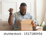 Small photo of African guy holds on lap carton box looks inside feels excited, man open unpack long-awaited parcel, satisfied online store client, trusted transport company, fragile goods delivered unscathed concept