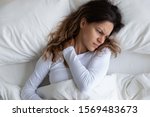 Small photo of Above view frown millennial woman feels pain in neck after night, awaken in bad temper having painful sudden ache or stiffness, concept of poor incorrect posture during sleeping or too soft mattress