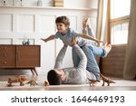 Joyful young man father lying on carpet floor, lifting excited happy little child son at home. Full length carefree two generations family having fun, practicing acroyoga in pair in living room.