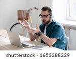 Small photo of Focused young businessman in eyewear wearing headphones, holding video call with clients on laptop. Concentrated millennial man in glasses giving online educational class lecture, consulting customer.