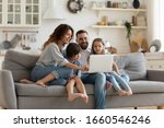Small photo of Happy young family with little kids sit on sofa in kitchen have fun using modern laptop together, smiling parents rest on couch enjoy weekend with small children laugh watch video on computer at home
