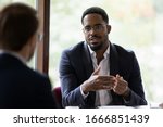 Confident concentrated African American male employee talk with colleague explain thought or idea, focused biracial businessman speak with coworker or partner, brainstorm at office boardroom meeting