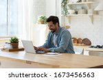 Small photo of Smiling young man working on laptop in modern kitchen, checking email in morning, writing message in social network, happy young male using internet banking service, searching information
