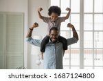 Small photo of Small son sit on strong dad shoulders showing biceps. African family enjoy activity games at home, healthy fit lifestyle, two superheroes, vitamins for adults and children ad, happy Father Day concept