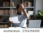 Small photo of Frustrated biracial male student sit at desk feel distressed with bad news in paper letter, unhappy African American man stressed by dismissal notice or negative reply in post correspondence or notice