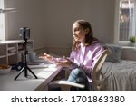 Teen girl blogger influencer recording video blog concept speaking looking at smartphone on tripod at home table. Teenager social media vlogger shooting vlog, streaming online podcast on mobile phone.