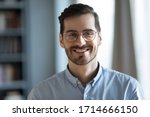 Head shot portrait close up smiling confident businessman wearing glasses looking at camera, standing in modern cabinet, successful happy young man, employee, worker in eyewear posing for photo