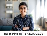 Head shot portrait smart confident smiling millennial indian woman standing with folded arms at home. Attractive young hindu teenager student girl freelancer looking at camera, posing for photo.