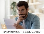 Small photo of Frustrated millennial guy in glasses read bad unpleasant news in postal letter, sad confused young man consider paperwork get negative answer in post correspondence, eviction or dismissal notice