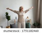 Overjoyed elderly 60s woman stand in living room stretching welcoming new sunny day, excited happy mature 50s female feel optimistic enjoy good leisure weekend relax rest in own cozy home