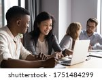 Multi-ethnic affiliates working on task together seated at desk in co-working, mature asian mentor teach new employee african guy, diverse mates having fun using laptop, learn corporate apps concept